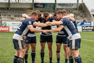 Joueurs de rugby en cercle avant un match de Fédérale 2, maillots bleu marine et blanc sur terrain enherbé